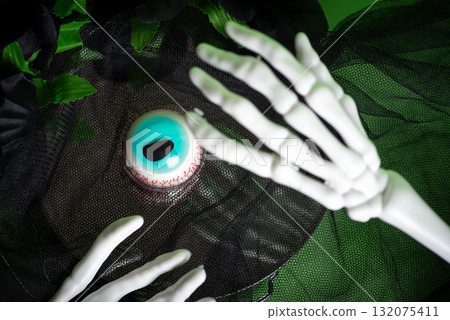 Skeleton hands displaying an eerie blue eyeball on a dark layer 132075411