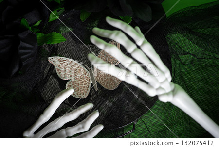 A skeleton hand reaches for an intricate butterfly surrounded by fabric 132075412