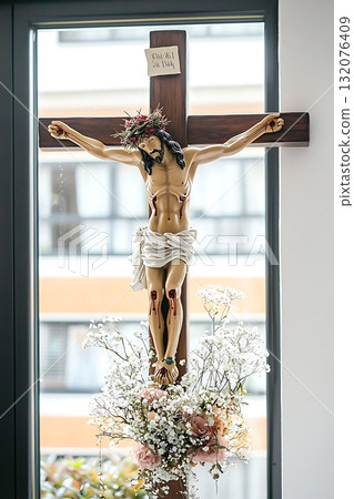 Wooden cross with a man on top of it and a flower arrangement below it 132076409