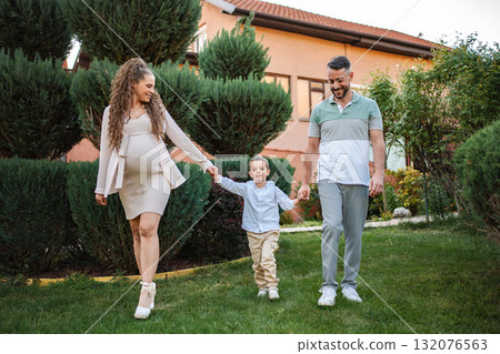 Expecting family enjoys a joyful stroll in green garden 132076563