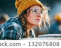 Young woman with glasses and yellow beanie gazing thoughtfully outdoors 132076808
