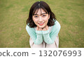 一位女士蹲在公園的草地上，微笑著抬頭 132076993
