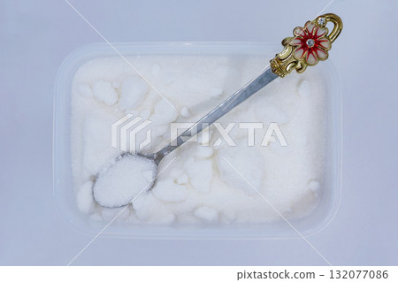 A plastic container filled with sugar with a small spoon A plastic container filled with sugar with a small spoon 132077086