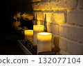Cozy interior with glowing candles and soft warm light on brick wall. Peaceful home atmosphere and evening relaxation concept 132077104