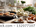 Home kitchen cooking scene with frying pan on induction cooktop, patties steaming, surrounded by fresh onions, dill, eggs, garlic, mushrooms, cheese, and spices in bright interior with copy space 132077107