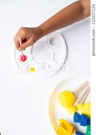 Child painting with colorful paints using wooden brushes on white palette 132077129