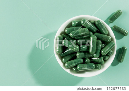 Green spirulina capsules in white bowl on mint background.Organic superfood supplement for detox, energy, immune support 132077383