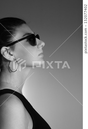 Black and white portrait. Beautiful, elegant woman wearing sunglasses, gazing into the distance Black and white portrait. Beautiful, elegant woman wearing sunglasses, gazing into the distance 132077402