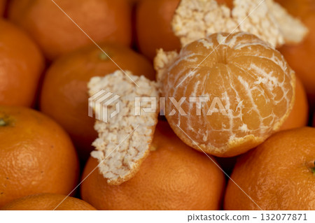 open tangerines are stacked together, a large number of ripe orange tangerines are on the table and several peeled tangerines are on top 132077871