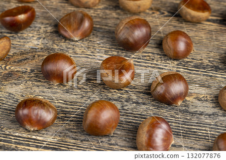 a hard chestnut fruit in a brown shell on a wooden table, a group of raw fruits of chestnut with a hard shell of brown color a hard chestnut fruit in a brown shell on a wooden table, a group of raw fruits of chestnut with a hard shell of brown color 132077876