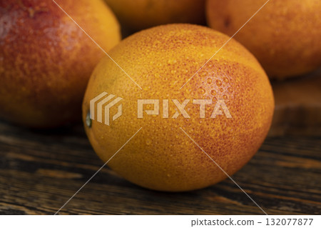 ripe fresh red-orange oranges with juicy flesh covered with drops of water on a wooden table, sweet and wet oranges with an unusual red color on the table 132077877