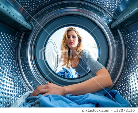 Woman doing laundry and looking inside washing machine with clothes on a sunny day at home Woman doing laundry and looking inside washing machine with clothes on a sunny day at home 132078130