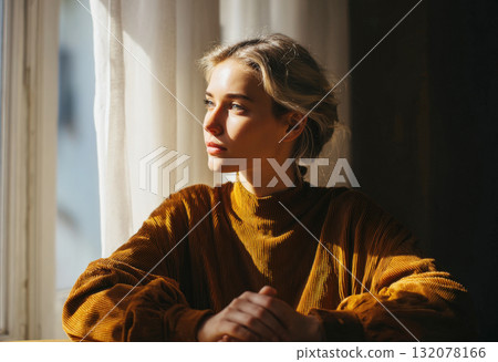Intimate and Pensive Portrait of a Young Woman with Backlit Blonde Hair, Wearing a Warm Corduroy Turtleneck, Sitting by a Window at Golden Hour, Capturing Solitude, Contemplation, Cozy Home Lifestyle 132078166