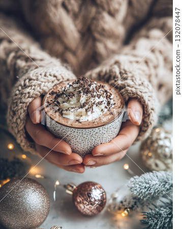 A close-up, vertical shot of hands in a chunky cable knit sweater holding a warm mug of hot chocolate or cocoa garnished with whipped cream and chocolate shavings. 132078447