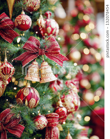 A richly decorated Christmas tree with a vertical focus on luxurious red and gold ornaments, textured ribbon bows, and a pair of golden bells. The background features a beautiful bokeh of warm lights A richly decorated Christmas tree with a vertical focus on luxurious red and gold ornaments, textured ribbon bows, and a pair of golden bells. The background features a beautiful bokeh of warm lights 132078454