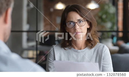 close-up portrait of a serious, focused businesswoman or hr manager in glasses, holding documents while listening or interviewing a person off-camera. Great for corporate, consultation themes. 132078560