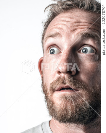 An intense, dramatic close-up portrait capturing a bearded man's face mid-expression. His eyes are wide and startled, looking up and to the side with an open mouth, conveying shock, surprise, fear 132078704