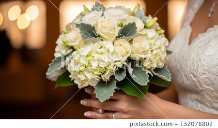 A hyper-realistic, high-detail close-up photograph of a bride's hands gently holding a gorgeous wedding bouquet filled with creamy white Hydrangeas, ivory Spray Roses, Dusty Mille 132078802
