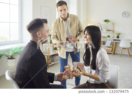 Woman with bouquet and gift as man proposes while another man looks surprised Woman with bouquet and gift as man proposes while another man looks surprised 132079475