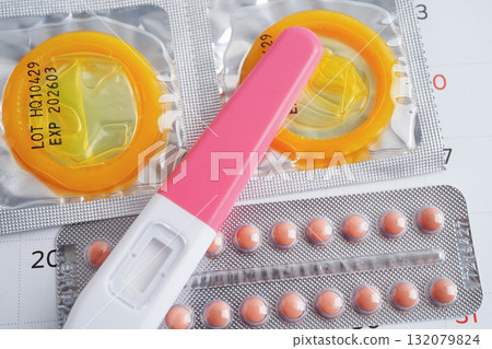 Pregnancy test with birth control pills and condom for female on calendar, ovulation day. Pregnancy test with birth control pills and condom for female on calendar, ovulation day. 132079824