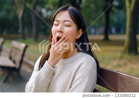 Woman yawning on a park bench 132080212