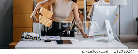 Asian woman prepares parcels and checks online orders on tablet and laptop for delivery online shopping and small business success 132080244