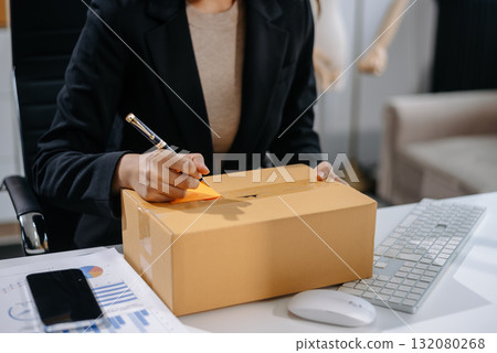 Asian woman prepares parcels and checks online orders on tablet and laptop for delivery online shopping and small business success 132080268
