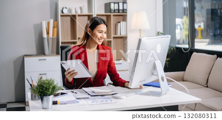 Young beautiful woman typing on tablet and laptop while sitting at the working white table in modern office 132080311