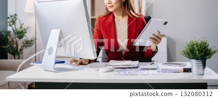 Young beautiful woman typing on tablet and laptop while sitting at the working white table in modern office Young beautiful woman typing on tablet and laptop while sitting at the working white table in modern office 132080312