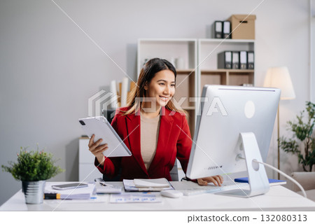 Young beautiful woman typing on tablet and laptop while sitting at the working white table in modern office 132080313