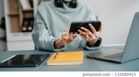Young Asian student studying at the college library, sitting at the desk, using a laptop computer, tablet and headphones having a video chat. 132080453
