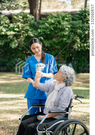 Asian physiotherapist helping elderly woman patient stretching arm during exercise correct with dumbbell in hand during training hand with patient Back problems in the garden. Asian physiotherapist helping elderly woman patient stretching arm during exercise correct with dumbbell in hand during training hand with patient Back problems in the garden. 132080657