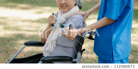 Asian physiotherapist helping elderly woman patient stretching arm during exercise correct with dumbbell in hand during training hand with patient Back problems in the garden. 132080673