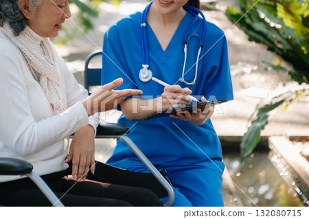 Elderly asian senior woman on wheelchair with Asian careful caregiver and encourage patient, walking in garden. 132080715