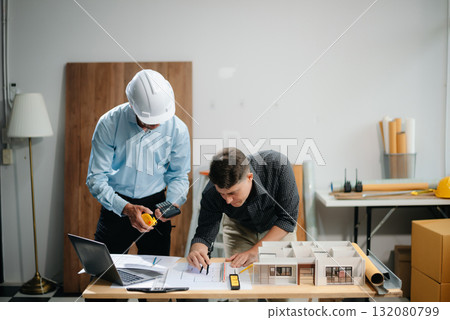 Contractor and architect looking at plan, tablet, laptop and talking about working on big project. Contractor and architect looking at plan, tablet, laptop and talking about working on big project. 132080799