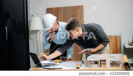 Contractor and architect looking at plan, tablet, laptop and talking about working on big project. Contractor and architect looking at plan, tablet, laptop and talking about working on big project. 132080802