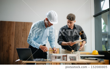 Contractor and architect looking at plan, tablet, laptop and talking about working on big project. 132080805