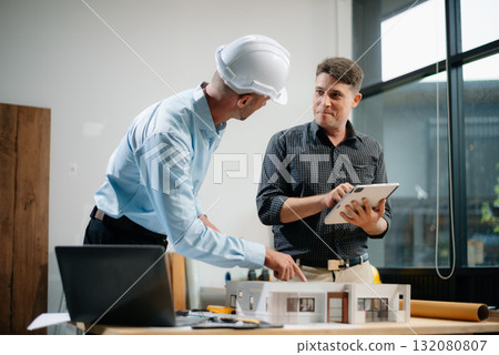 Professional collaboration in architecture. Two engineers work on construction plans, using tools like laptops, tablets, and scale models. Professional collaboration in architecture. Two engineers work on construction plans, using tools like laptops, tablets, and scale models. 132080807