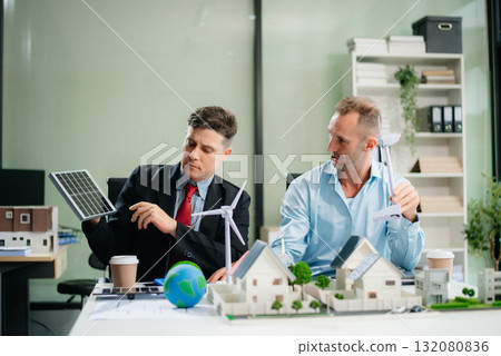 Experts collaborate on renewable energy solutions with house models, wind turbines, and solar panels, emphasizing green design 132080836