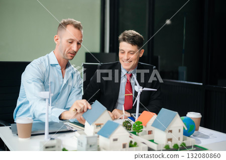 Experts collaborate on renewable energy solutions with house models, wind turbines, and solar panels, emphasizing green design 132080860