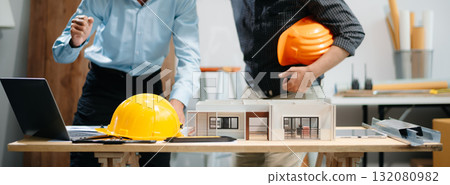 Professional collaboration in architecture. Two engineers work on construction plans, using tools like laptops, tablets, and scale models. 132080982