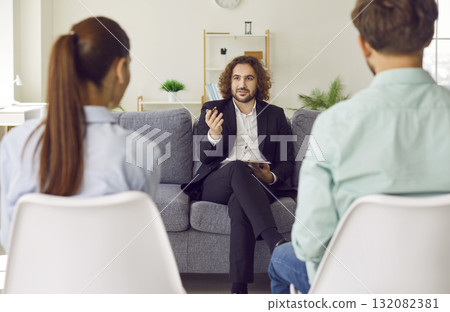 Young couple sitting back on chairs and listening to psychologist on therapy session. 132082381