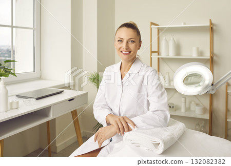 Young smiling woman cosmetologist sitting in beauty spa salon on workplace and looking at camera. 132082382