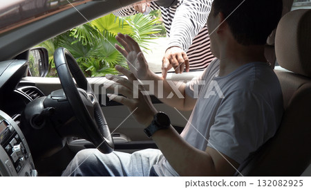 Masked thief threatening a driver through a car window during an attempted robbery. Concept of car crime, carjacking, danger, security awareness, and personal safety in urban environments Masked thief threatening a driver through a car window during an attempted robbery. Concept of car crime, carjacking, danger, security awareness, and personal safety in urban environments 132082925