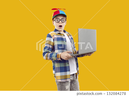 Surprised boy in funny glasses and colored cap with propeller looks directly into the camera, dressed in plaid shirt and gray jeans. Surprised boy in funny glasses and colored cap with propeller looks directly into the camera, dressed in plaid shirt and gray jeans. 132084278