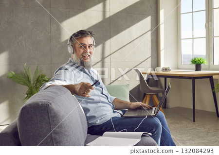 Middle aged man in headphones using laptop at home Middle aged man in headphones using laptop at home 132084293