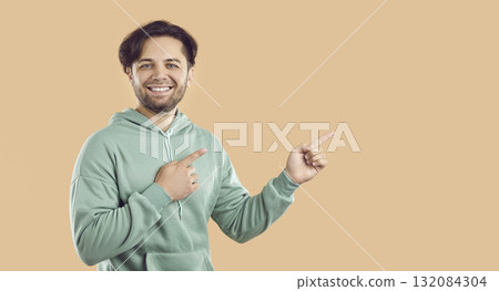 Happy man advertising casual fashion sale and pointing at copy space on beige background 132084304