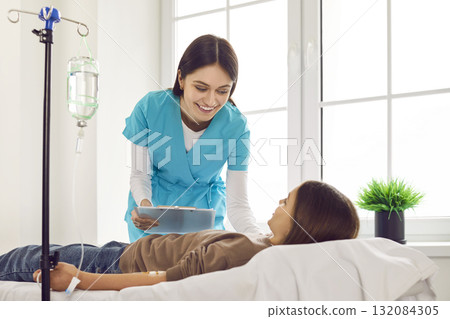 Teenage child girl lying on couch in clinic while receiving IV drip infusion and vitamin therapy. Teenage child girl lying on couch in clinic while receiving IV drip infusion and vitamin therapy. 132084305