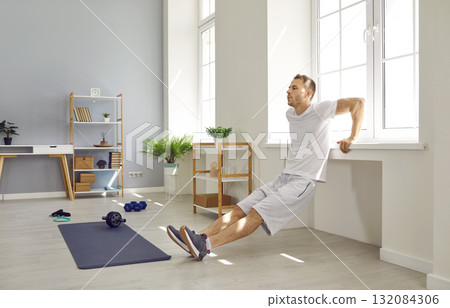 Fit, strong man doing triceps dips by window sill during fitness workout at home Fit, strong man doing triceps dips by window sill during fitness workout at home 132084306