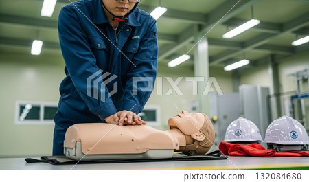 Asian female instructor wearing blue uniform performing chest compressions on CPR training mannequin in modern medical education facility with hard hats nearby Asian female instructor wearing blue uniform performing chest compressions on CPR training mannequin in modern medical education facility with hard hats nearby 132084680